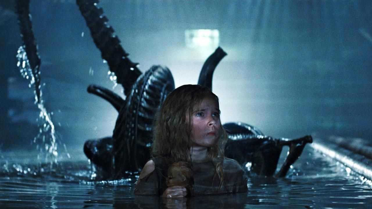 Child Carrie Henn wades in the water with her little doll while a giant disgusting alien emerges behind her.