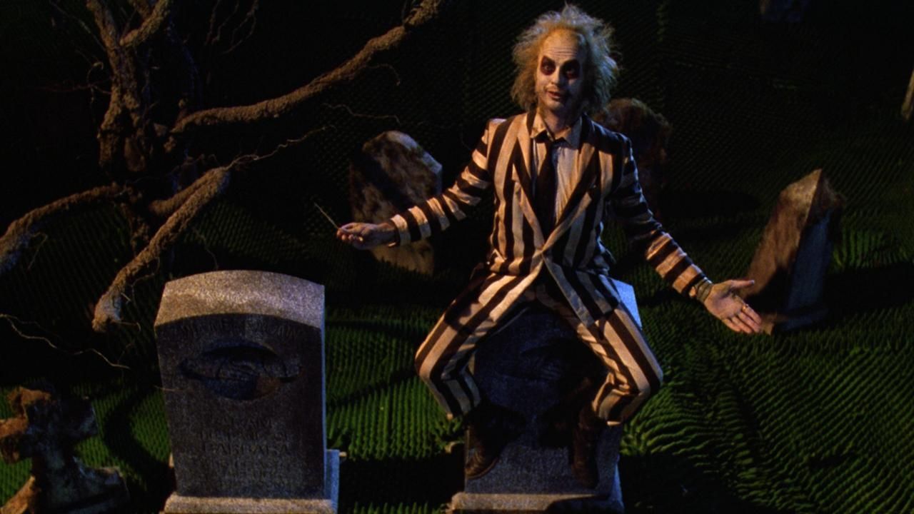 Michael Keaton sits on a tombstone as the titular Beetlejuice