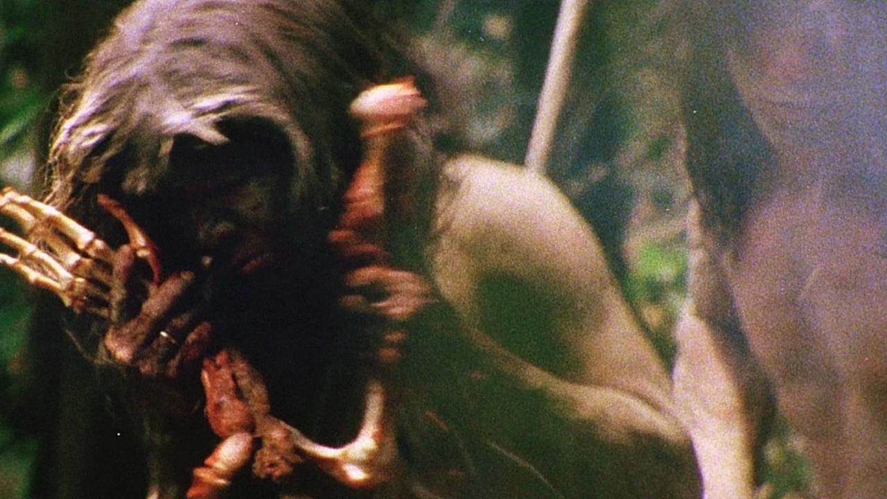An unnamed cannibal eats a bloody human arm in Cannibal Holocaust