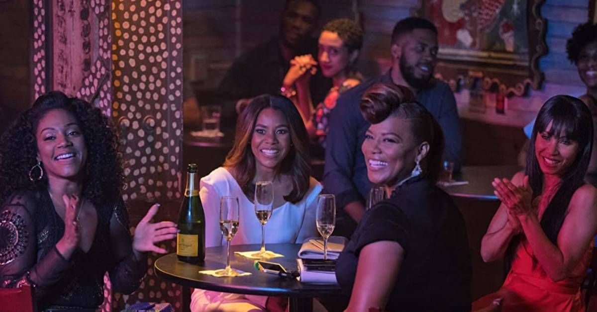 Tiffany Haddish, Regina Hall, Queen Latifah and Jada Pinkett Smith sit at a table together during an indoor scene from "Girls Trip" (2017).