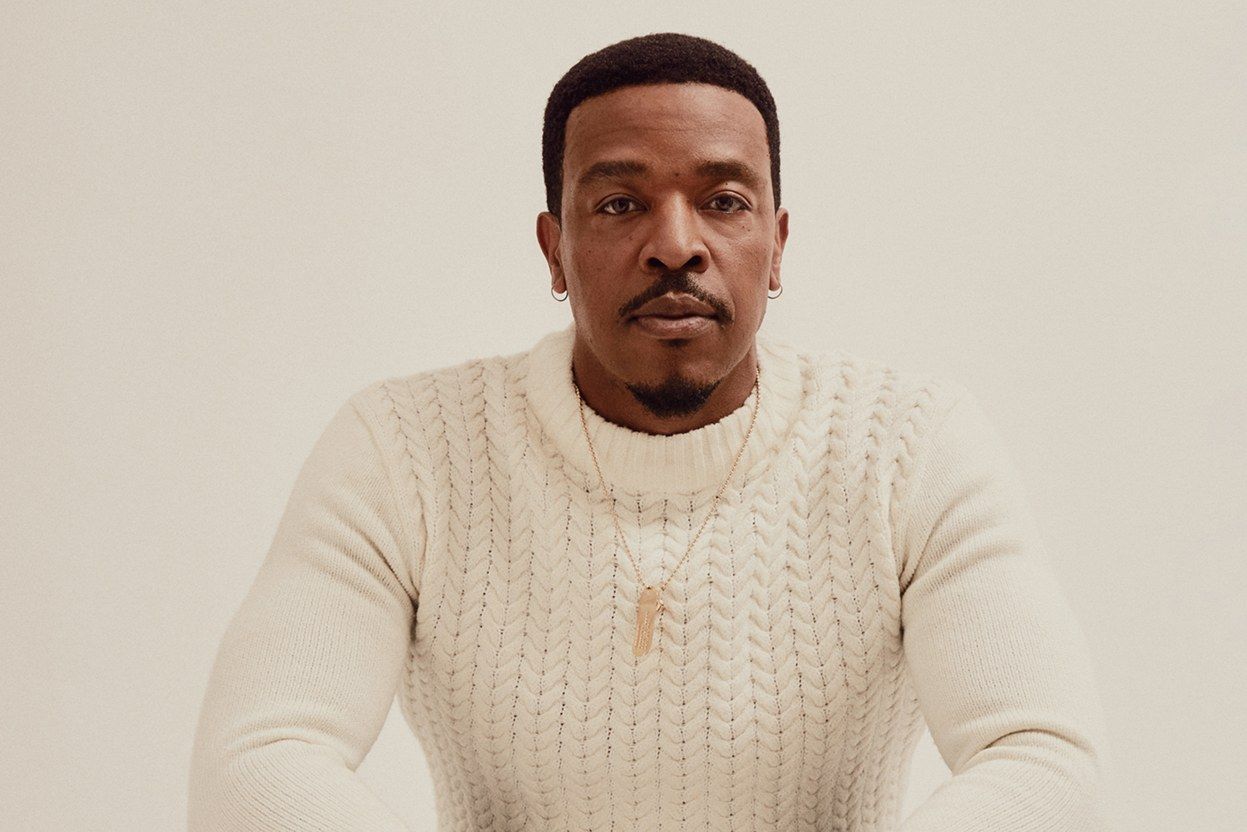 Russell Hornsby crouches in a white sweater