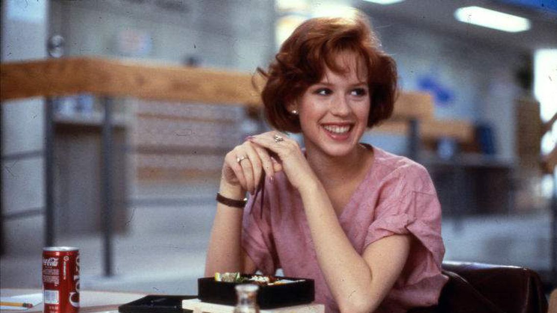 An image of (Claire) looking off into the distance and smiling amidst a plate of sushi, as part of a scene from The Breakfast Club. 