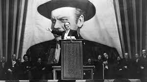Orson Welles standing at a podium in Citizen Kane. 