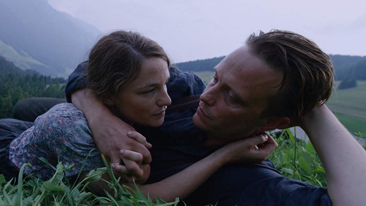 A couple lays in a field together, hands clasped as they look at each other