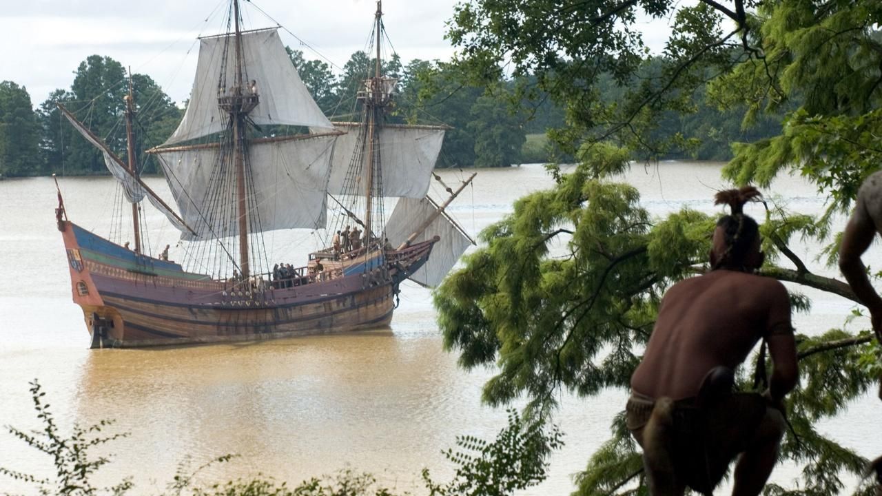 A large boat sails towards land while a native american watches from behind tree cover