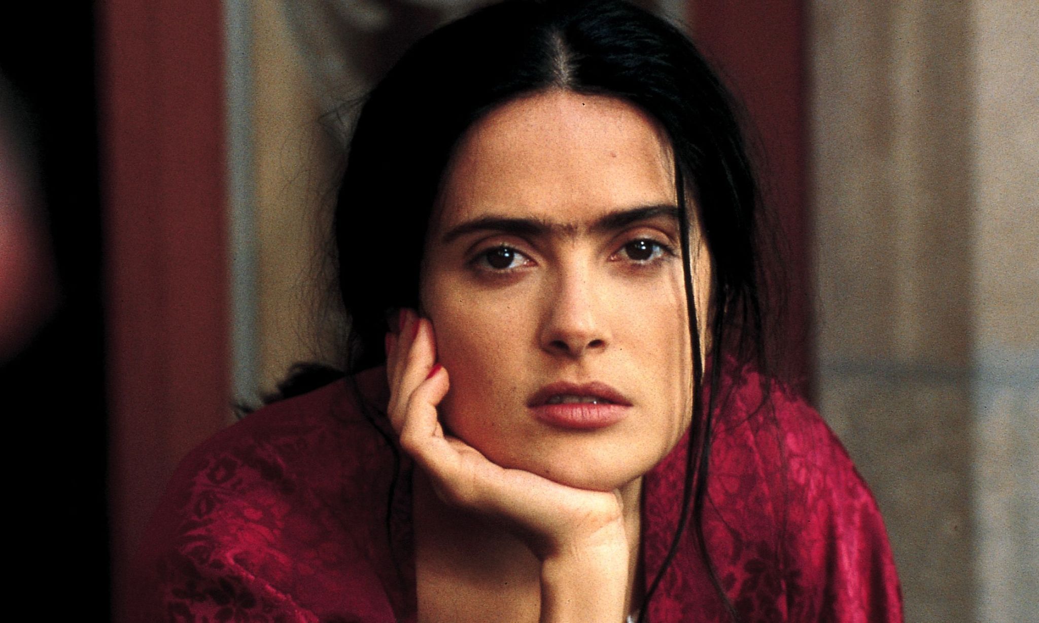 Woman (looks like Frida Kahlo) looks at camera with hand propped under chin.