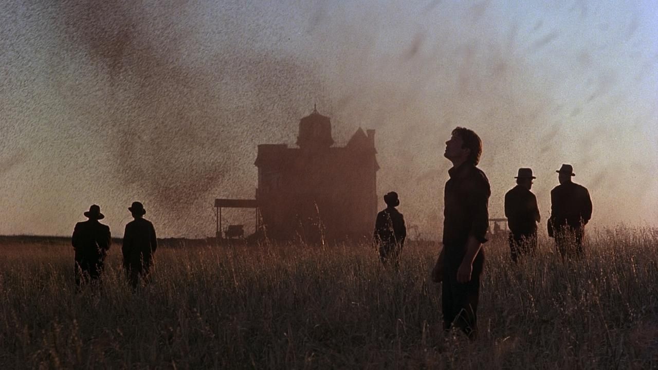 Several silhouetted people stand in a field while a house burns in the background.