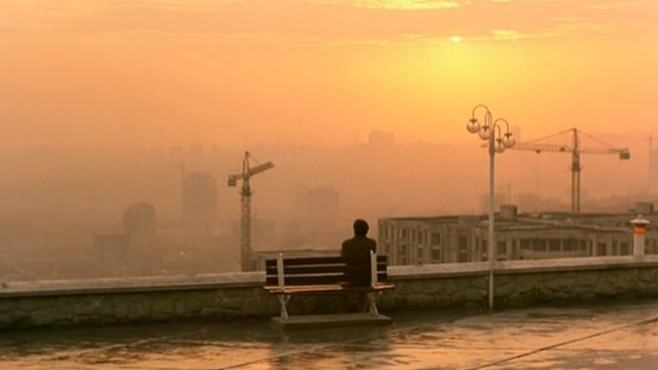 A man sits on a bench looking at the hazy orange skyline