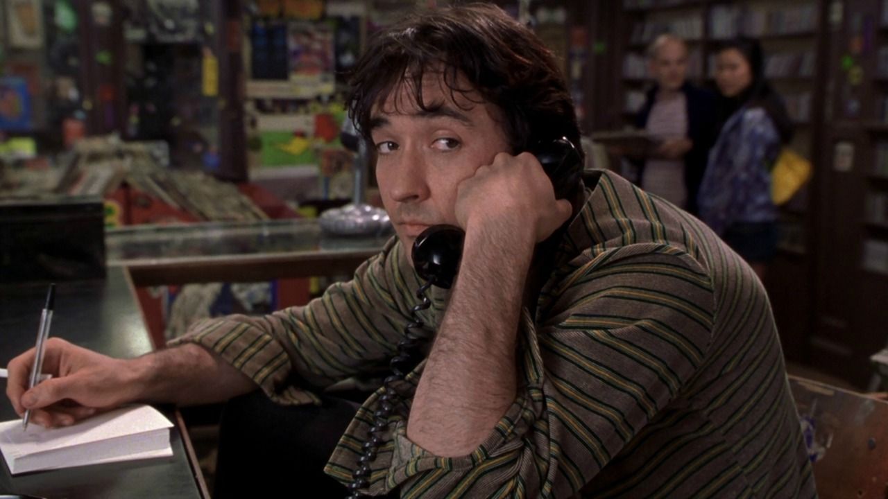 John Cusack answers the phone in a bored way but glances to the side 