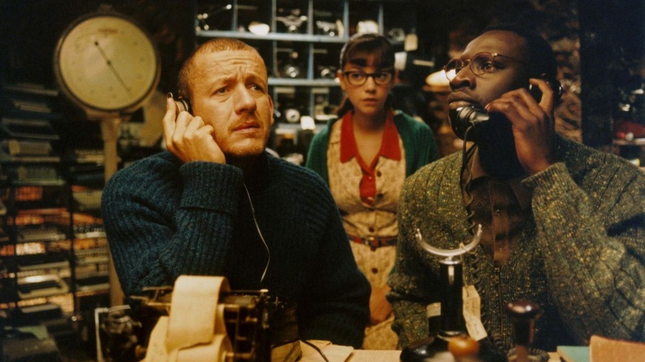 Three characters of Micmacs in a store, while two of them listen to phone recievers.