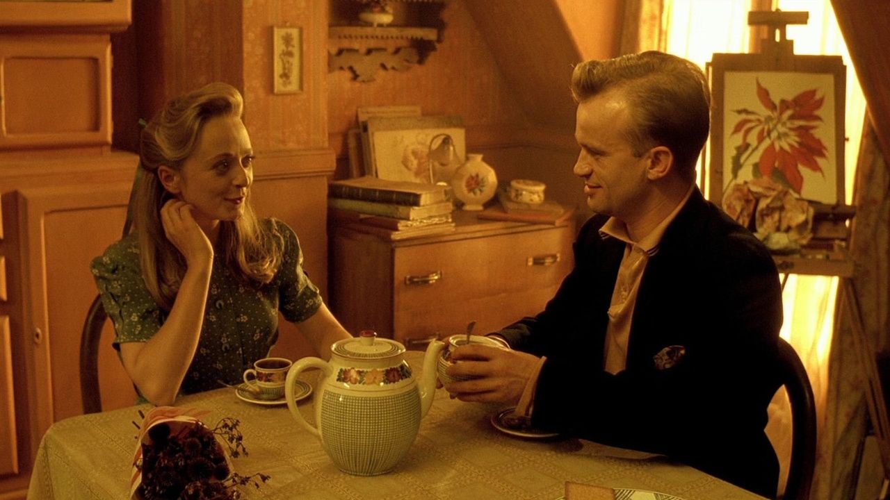 Two characters from Delicatessen smiling at one another as they sit at a dining table together.