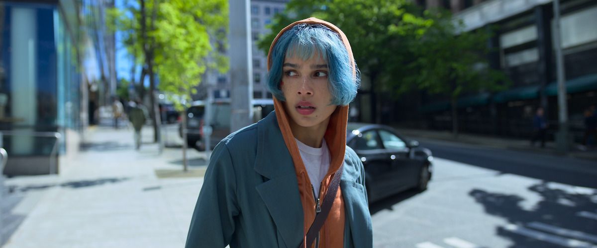 Woman with blue hair and orange hood up walks through streets.