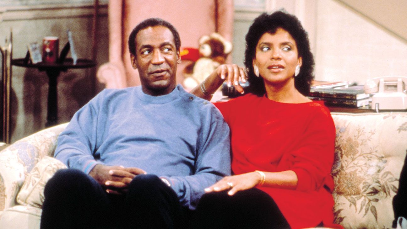 Dr. Huxtable (Bill Cosby) looks to the side on the couch with his wife