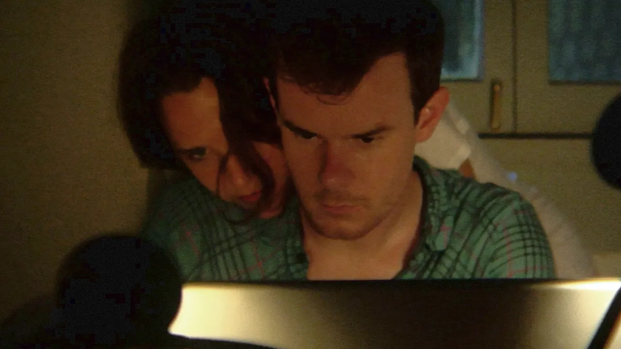 Joe Swanberg looking down at an open computer screen with a woman over his shoulder