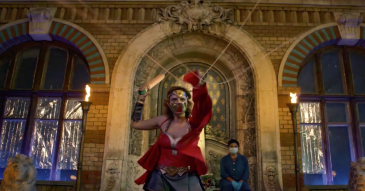 A woman in a weird mask and red suit holds a knife in an ornate building in Bad Luck Banging