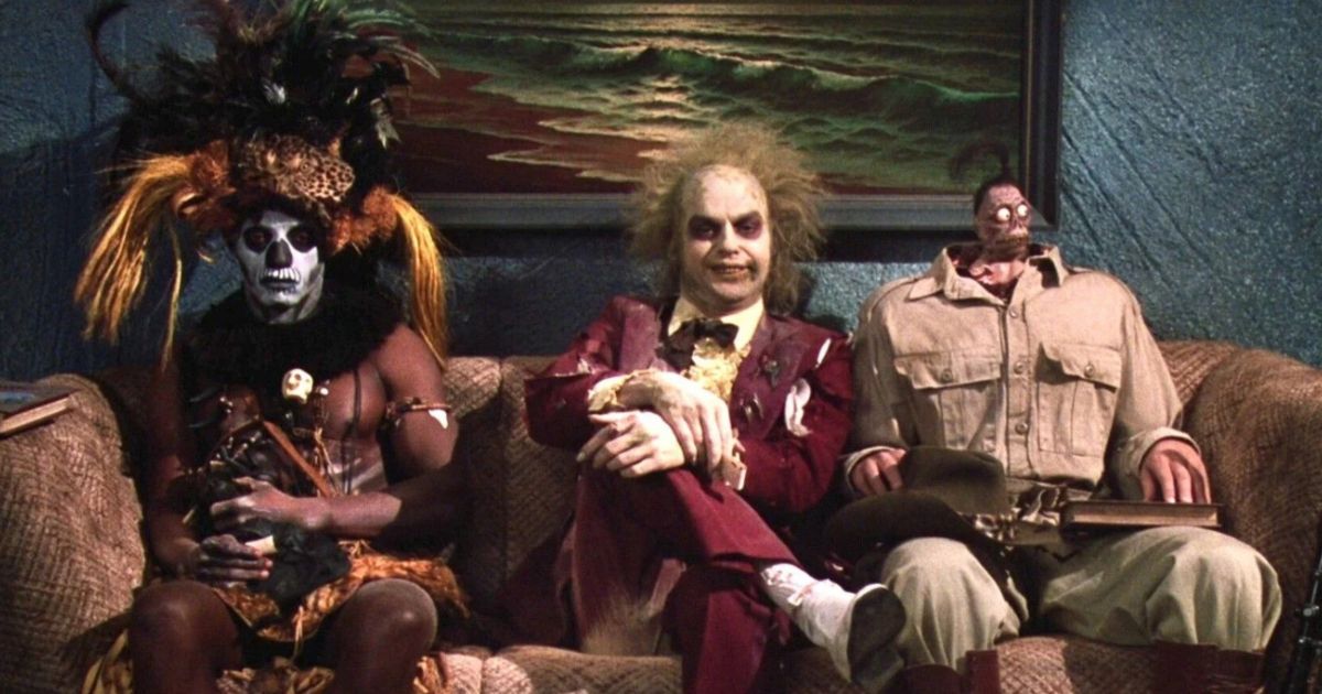 Beetlejuice sits in between two weird figures in the waiting room of the afterlife