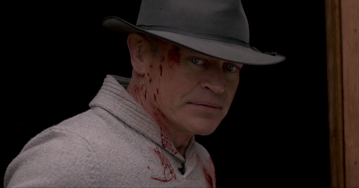 Boon in his hat and sweater, covered in blood, looks at the camera