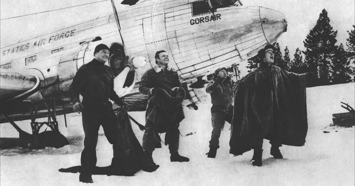 The cast in the snow by their plane in Island in the Sky