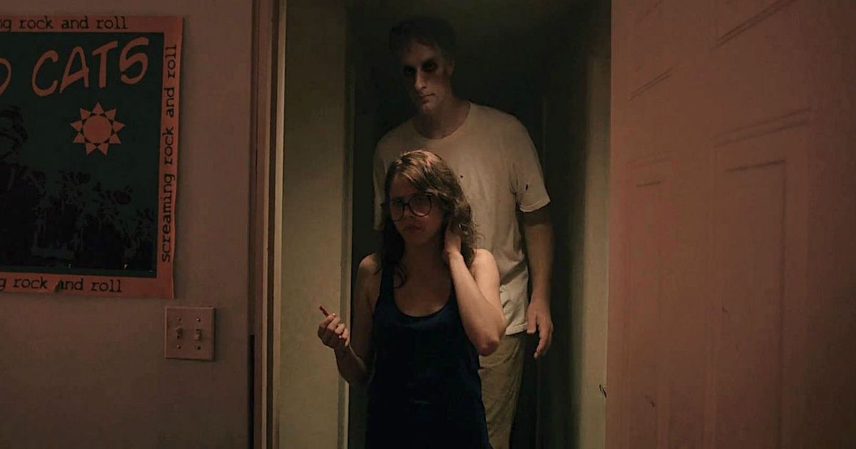 The tall man stands behind a girl in a doorway in It Follows