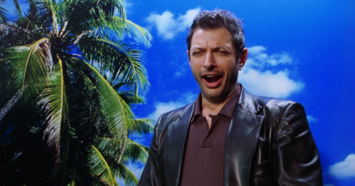 Jeff Goldblum yawns in a leather jacket against a fake blue cloud backdrop in Jurassic Park
