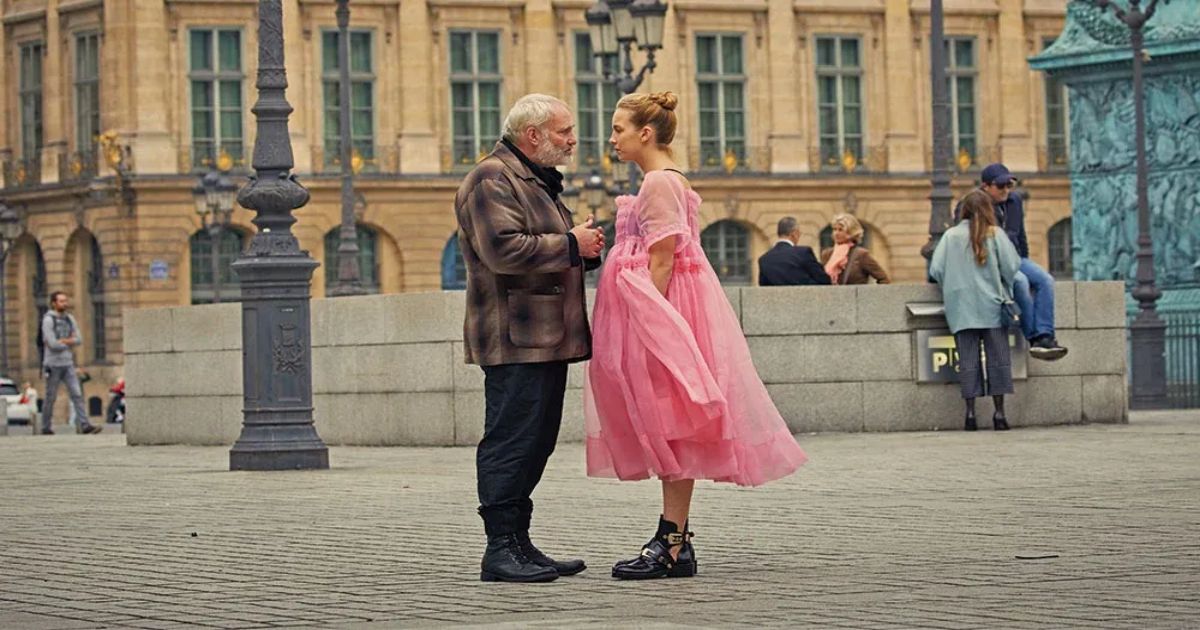 Villanelle (Jodie Comer) conversing seriously with Konstantin (Kim Bodnia) in a busy plaza in Killing Eve (2018). 