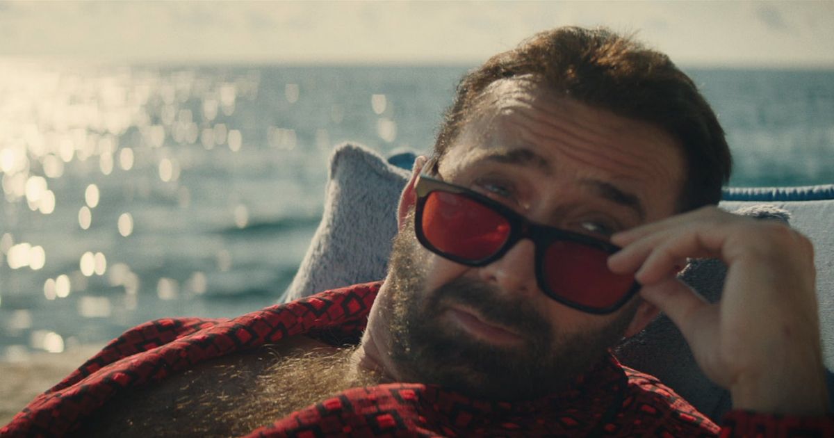 Nic Cage lowers his red sunglasses by the water in The Unbearable Weight of Massive Talent