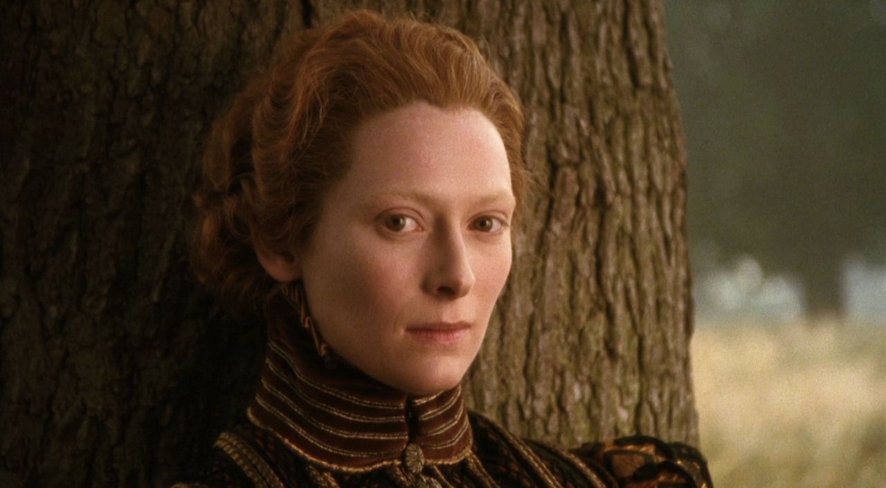 Close shot of Swinton standing against a tree with a slight smile in the film Orlando
