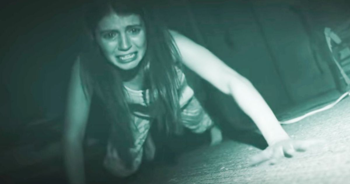 Uma mulher rasteja em direção à câmera com medo em Atividade Paranormal Next of Kin