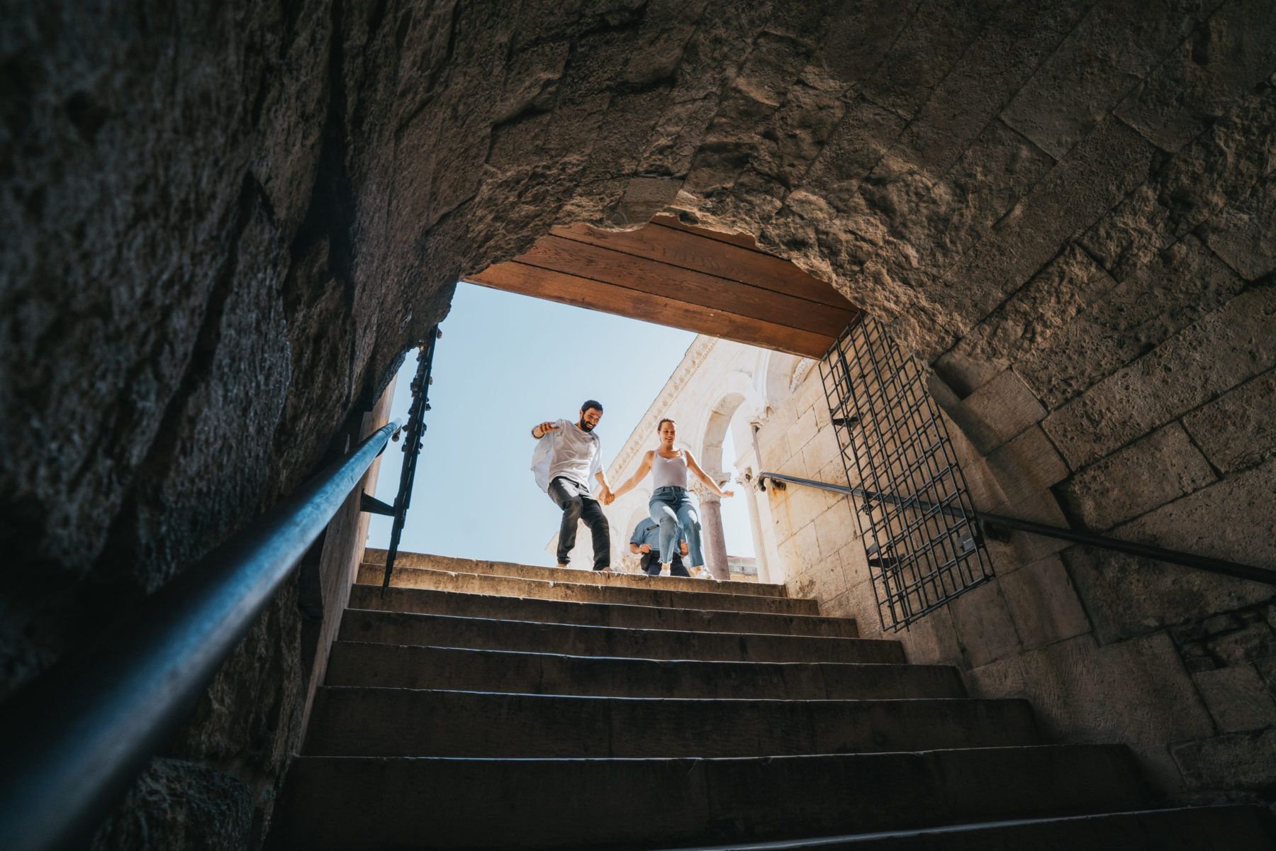 Man and woman hold hands as they run down steps frantically.