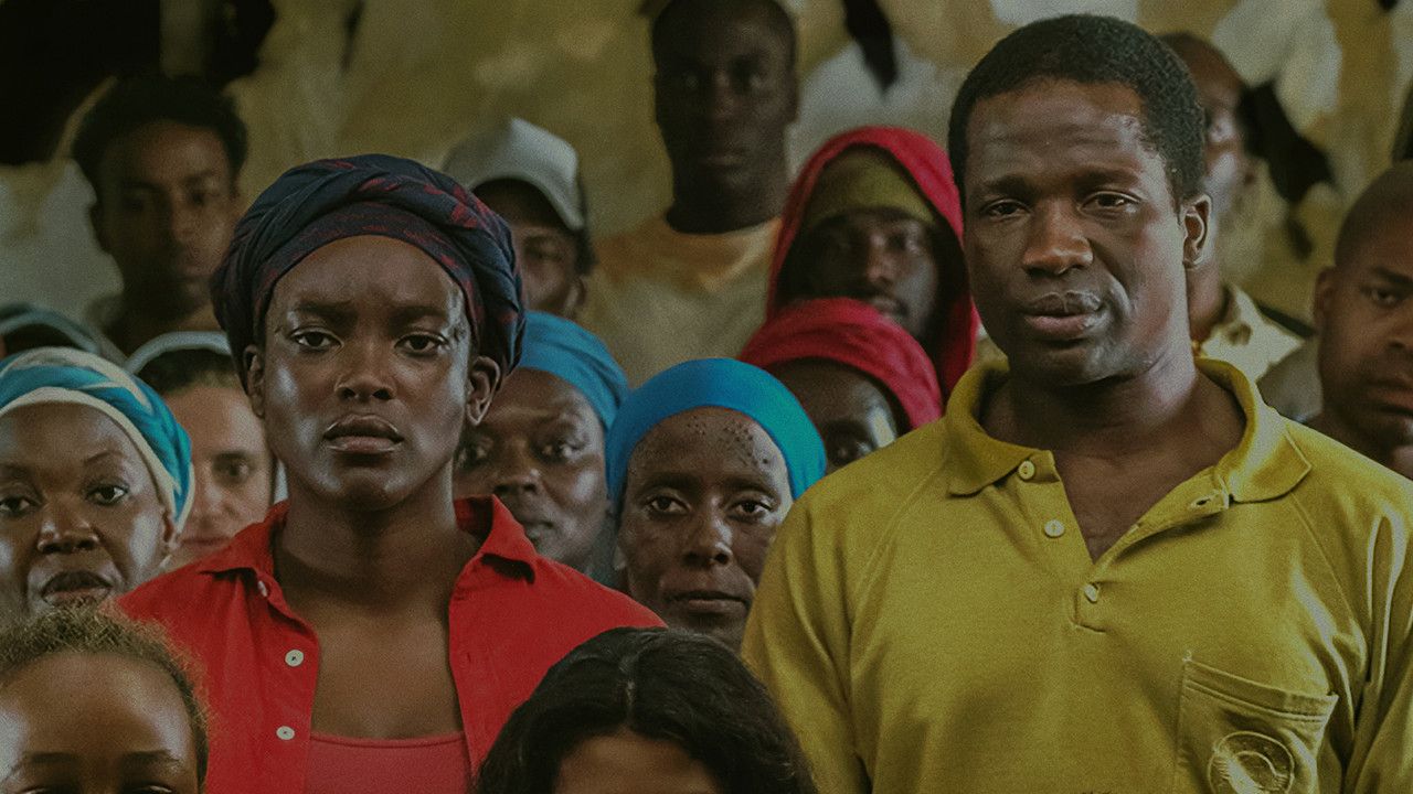 The main couple stands amidst a mass of Sudanese refugees in His House