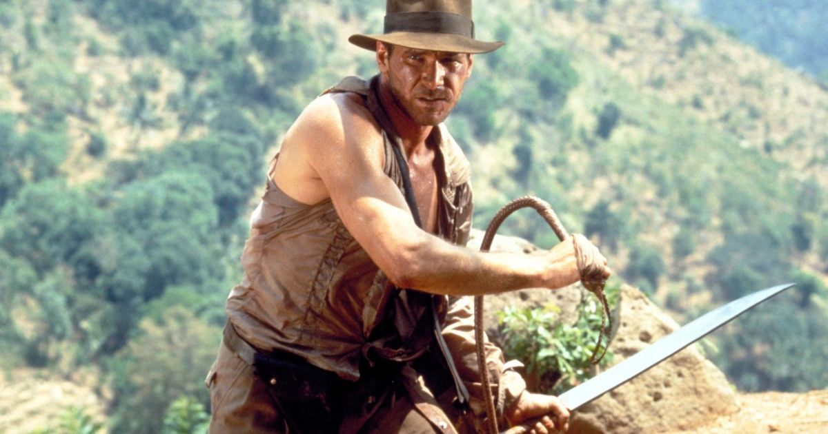 Harrison Ford as Indiana Jones with a sword in one hand and a whip in the other.