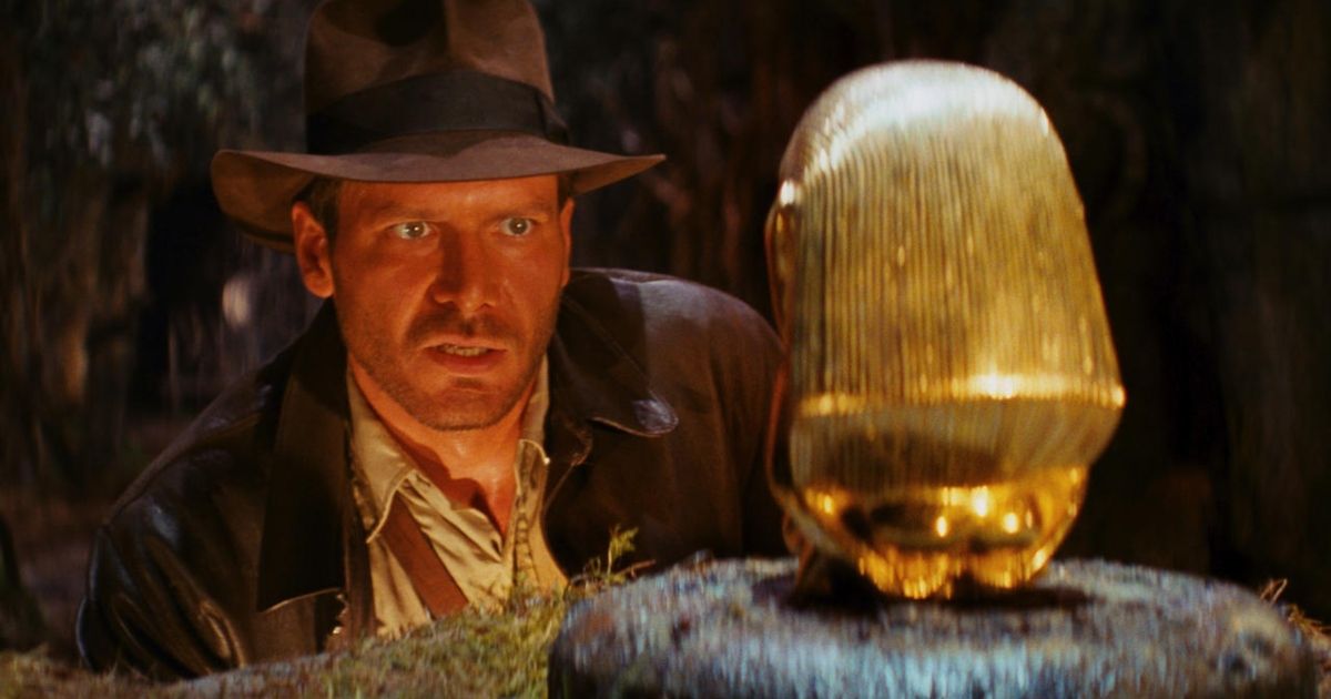 Indiana Jones at eye level with a golden idol, the idol facing away from the camera.