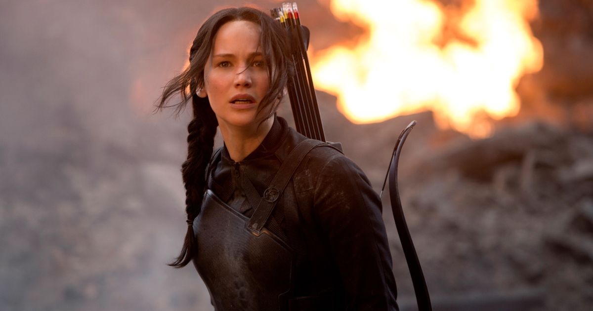 Jennifer Lawrence as Katniss Everdeen with a bow and arrow as a fire rages behind her.