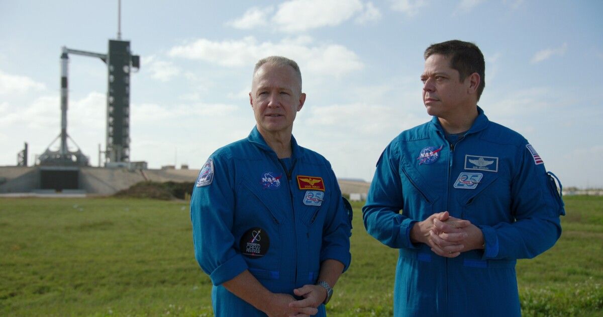 Two astronaut stand in front of terminal.
