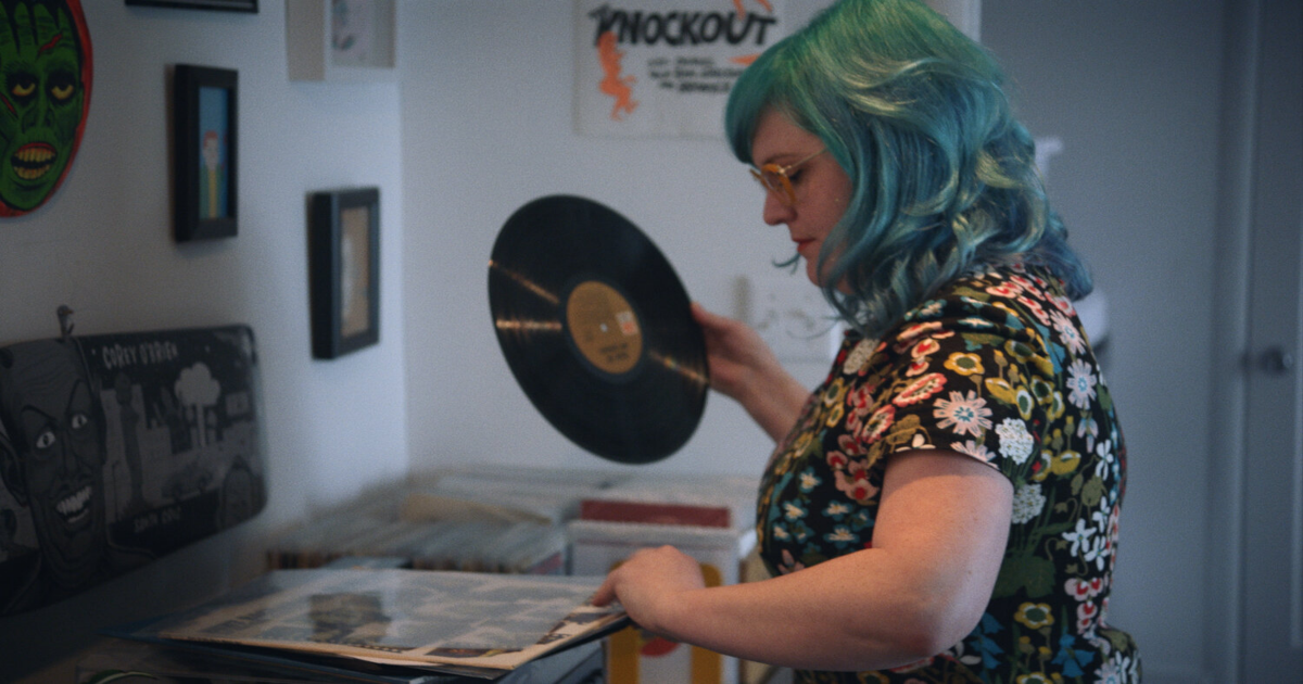 A woman with green hair holds a shiny viny record in Vinyl Nation
