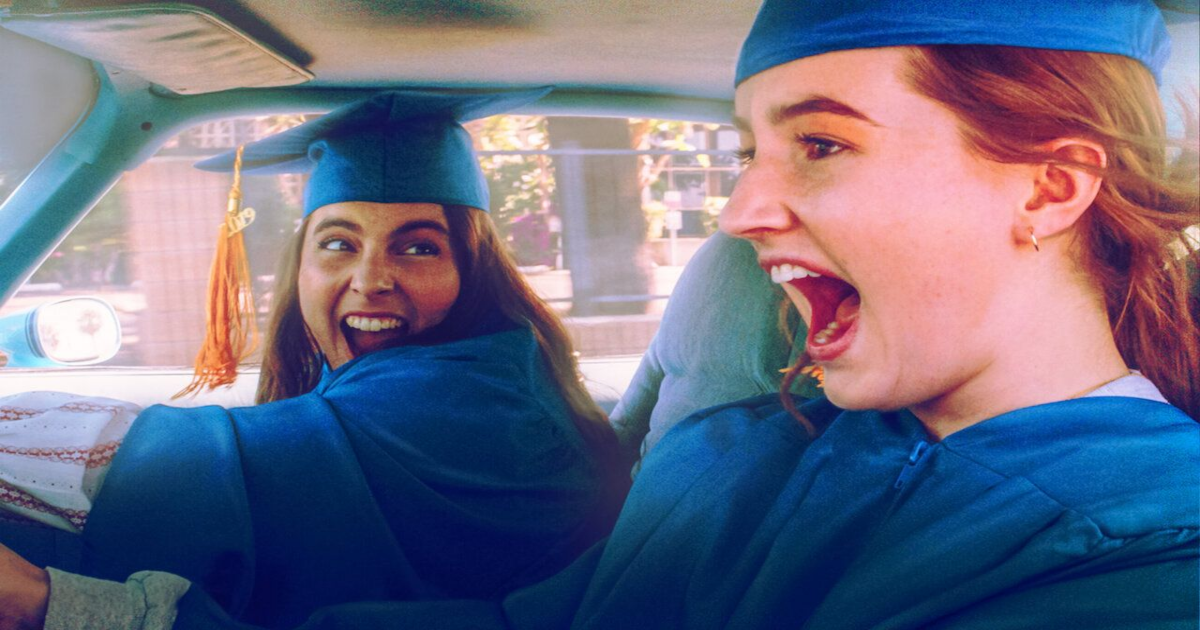Two girls speed away from high school wearing their blue graduation outfits in Booksmart