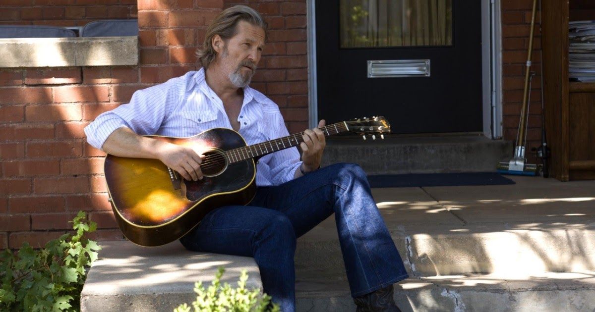 Man sits on doorstep with guitar.