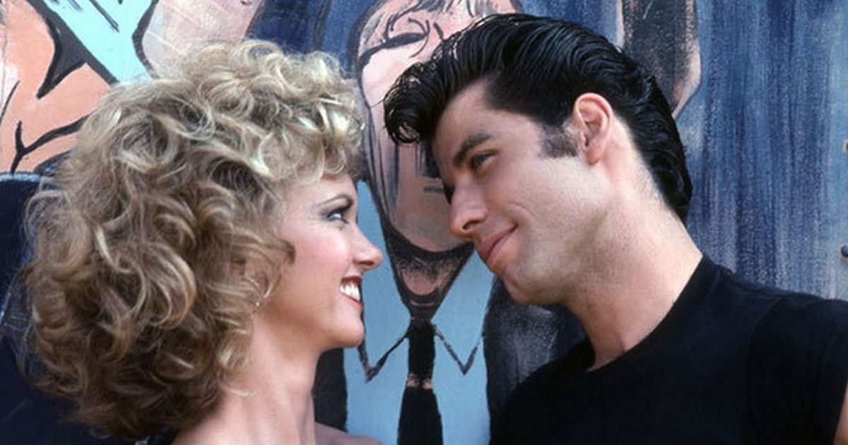 Sandy and Danny smiling at one another in front of a wall mural.