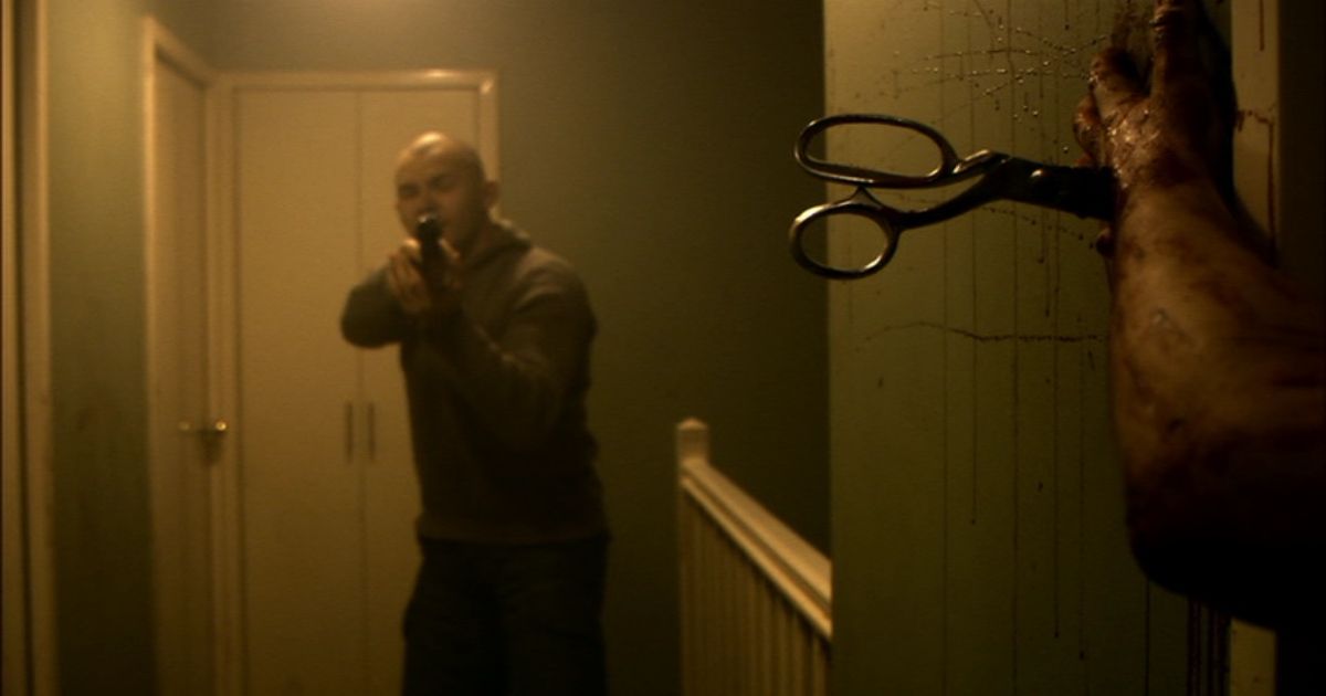 Un hombre apunta con un arma a alguien con unas tijeras clavadas en la mano en la pared en Inside