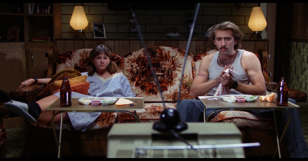 Holly Hunter and Nicolas Cage sit on a couch and watch TV in Raising Arizona