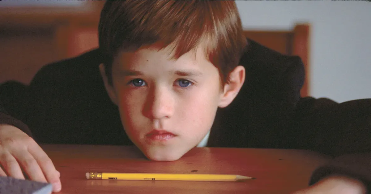 Boy puts chin on table, pencil is in front of him. He looks sad.