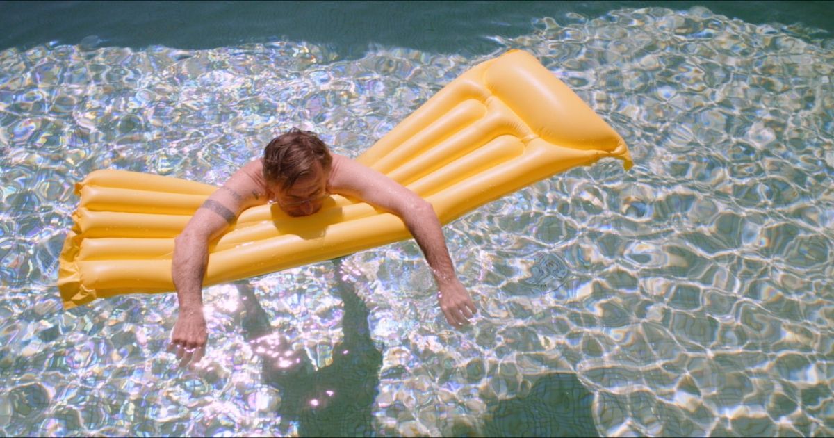 Tim Roth laying face down on a raft in a pool in Sundown