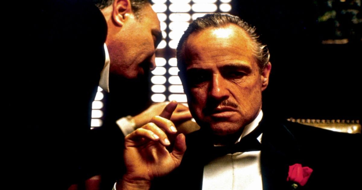 A man whispers into Marlon Brando's ear in The Godfather