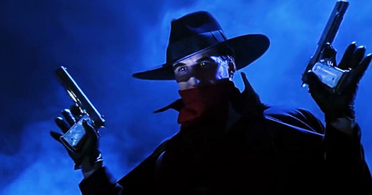 Alec Baldwin with two guns dressed as The Shadow in blue light