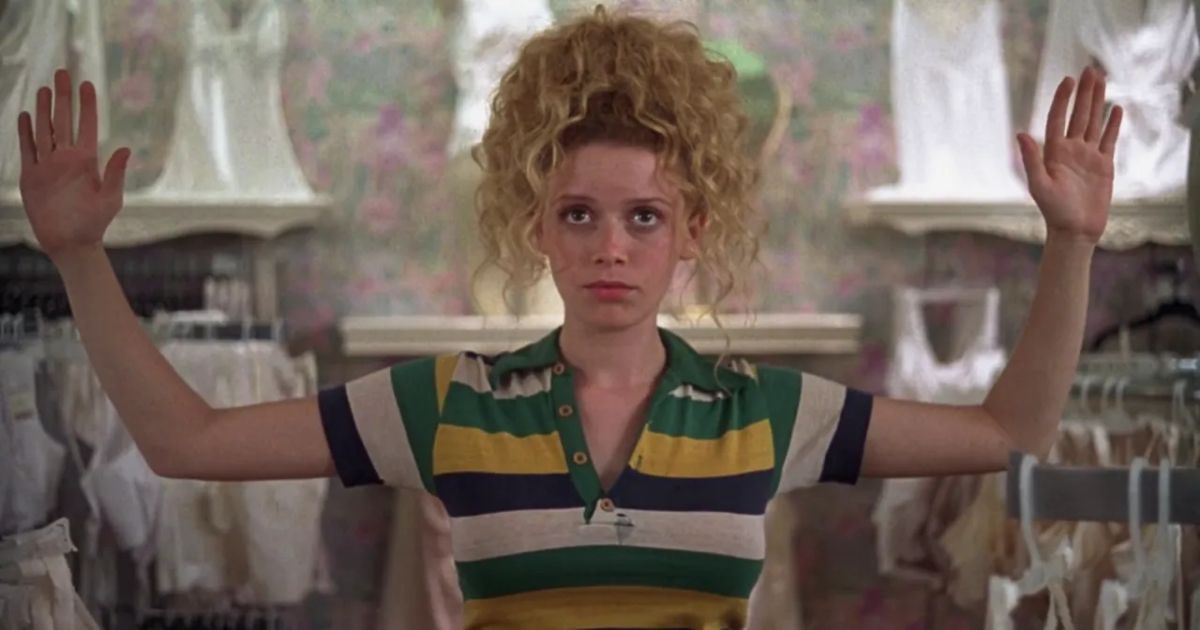Lyonne raises her hands up in a green yellow and white polo shirt in The Slums of Beverly Hills