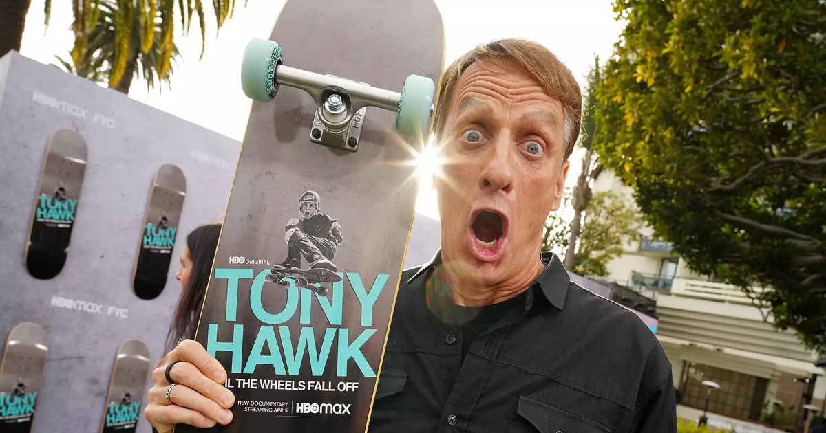 Tony Hawk holds a skateboard with the documentary title Until the Wheels Fall Off 