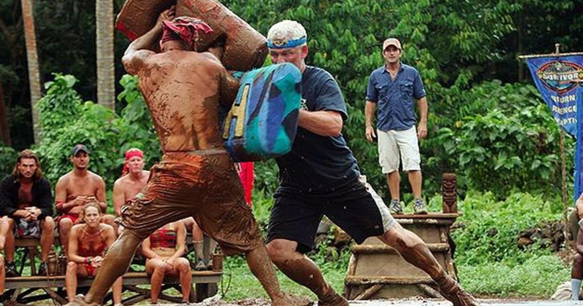 Two heroes vs villains contestants covered in mud as they push each other wish large mats.