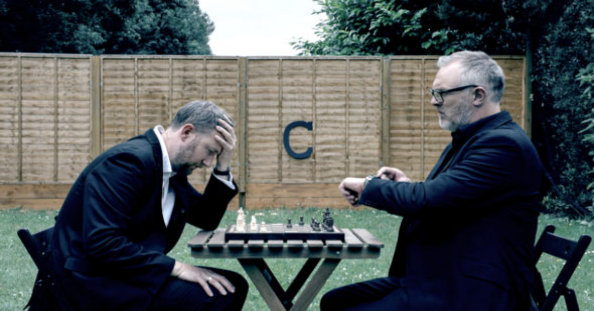Two men in suits play chess in a yard in Taskmaster
