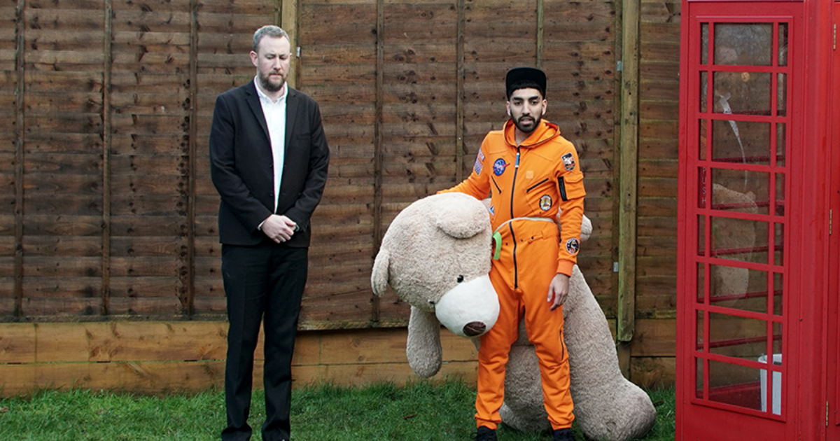 A man in a space suit with a large stuffed animal and a phone booth in Taskmaster