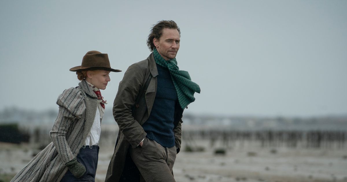 Man and woman walk along barren land in Victorian garb.